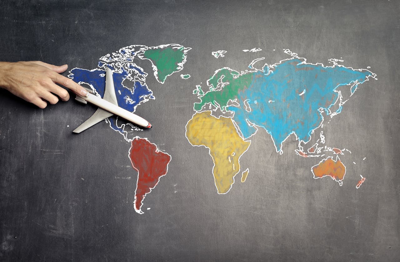 Top view of crop anonymous person holding toy airplane on colorful world map drawn on chalkboard